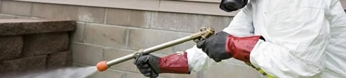Pest control technician applying exterior insect treatment along a home foundation in Tulsa, OK