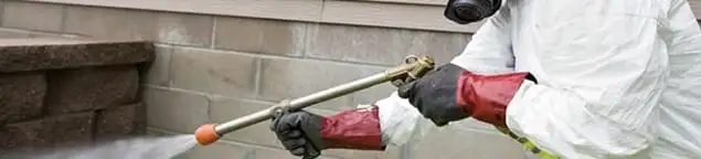 Pest control technician applying exterior insect treatment along a home foundation in Tulsa, OK