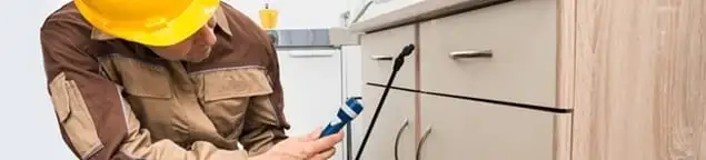 Roach exterminator applying treatment under kitchen cabinets in Tulsa, OK