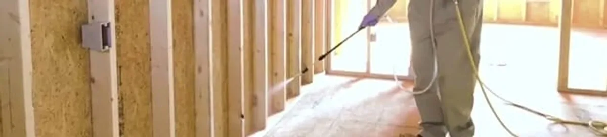 Termite treatment technician applying spray along framing and unfinished walls in Tulsa, OK