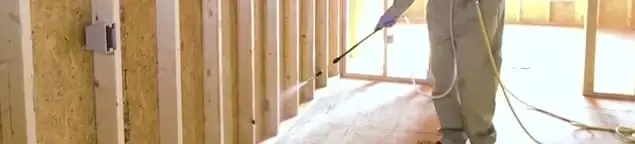 Termite treatment technician applying spray along framing and unfinished walls in Tulsa, OK